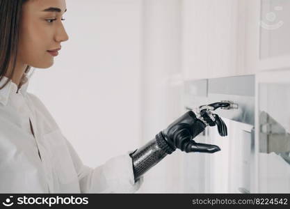 Modern disabled girl with robotic hand switching oven on, close-up. Young woman with bionic prosthetic arm cooking at home using artificial limb to turn on appliance. Disability and domestic life.. Modern disabled girl with bionic prosthetic arm turns oven on, cooking in kitchen at home, close up