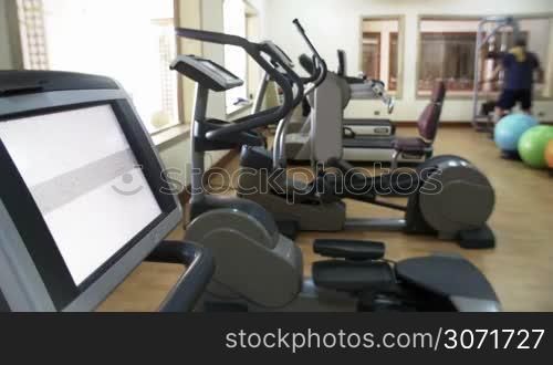 Modern fitness center with different types of exercise machines. Display with Touch the screen text in foreground. Man working out in background