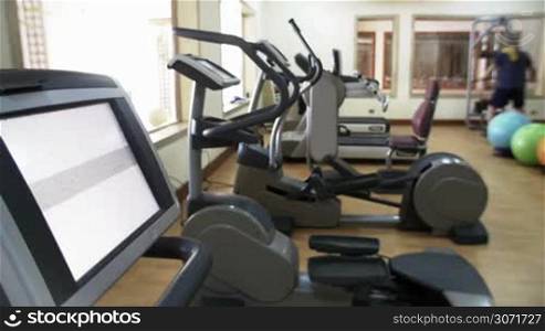 Modern fitness center with different types of exercise machines. Display with Touch the screen text in foreground. Man working out in background