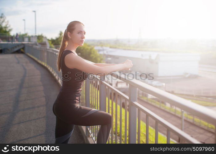 Modern fitness life. A woman in sportswear doing fitness exercises. City in sunny evening.