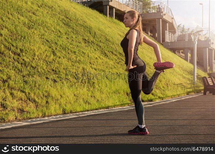 Modern fitness life. A woman in sportswear doing warming-up exercises. City in sunny evening.