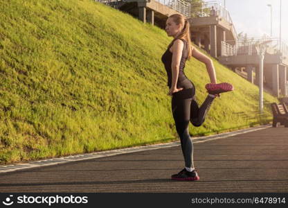 Modern fitness life. A woman in sportswear doing warming-up exercises. City in sunny evening.