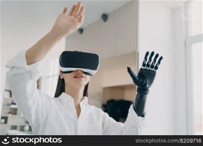 Modern girl in VR glasses interacting with augmented reality, using bionic prosthetic arm. Disabled young woman touching virtual objects by artificial limb. High tech in medicine and healthcare.. Modern disabled girl in VR glasses interacting with augmented reality, using bionic prosthetic arm