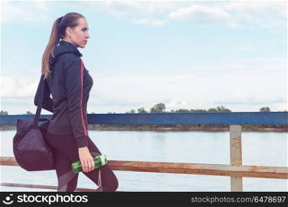 Modern healthy lifestyle. A woman in sportswear with bottle of water on embankment background