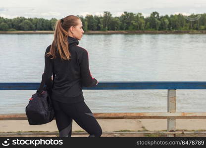 Modern healthy lifestyle. A woman in sportswear with bottle of water on embankment background