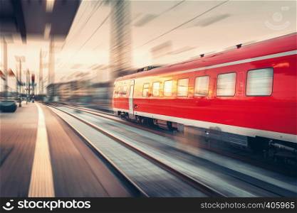 Modern high speed red passenger commuter train at the railway platform at sunset. Railway station in Nuremberg, Germany. Railroad with motion blur effect. Industrial concept landscape. Transportation
