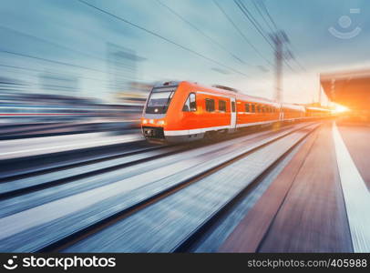 Modern high speed red passenger commuter train in motion at the railway platform at sunset. Railway station. Railroad with motion blur effect. Industrial landscape with train. Vintage toning