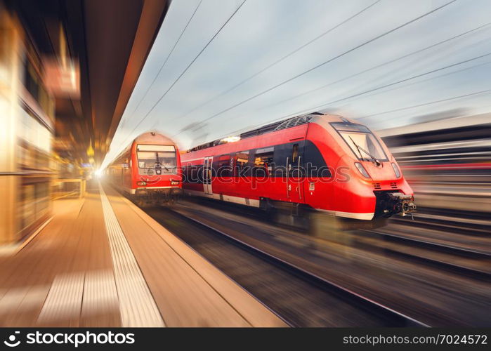 Modern high speed red passenger trains at sunset. Railway station in Nuremberg, Germany. Railroad with motion blur effect. Industrial concept landscape