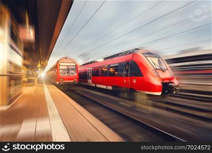 Modern high speed red passenger trains at sunset. Railway station in Nuremberg, Germany. Railroad with motion blur effect. Industrial concept landscape