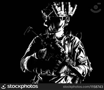 Modern infantry soldier, special operations forces tactical group shooter armed submachine gun with silencer, equipped radio headset and quad-tube night vision device standing in darkness, desaturated. Modern army elite forces shooter in darkness