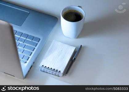 Modern laptop on evening work place, coffee cup and notebook with pen, view from above