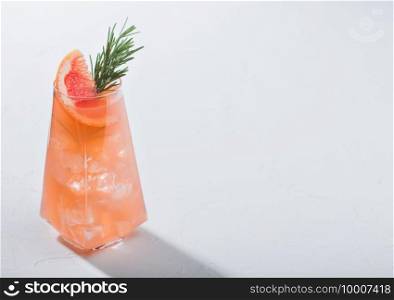 Modern luxury glass of refreshing summer red grapefruit cocktail with ice cubes, fruit slice and rosemary on white background. Space for text