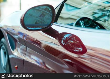 Modern luxury red sport car with beautiful reflections. Outdoors, exterior details, door, mirror, windows. Motion blur. Selective focus close up image. Auto show, street drive concept