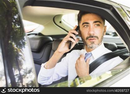 modern man sitting car adjusting his neck tie talking mobile phone