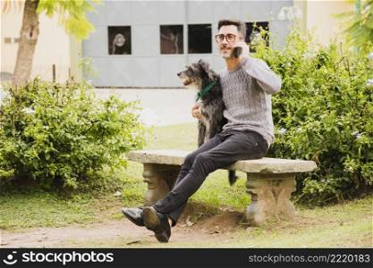 modern man sitting park with his dog talking mobile phone
