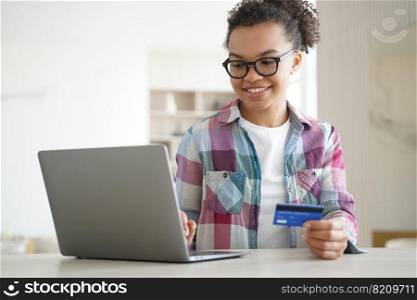 Modern mixed race teen girl holds bank credit card uses online banking services on laptop. Smiling young biracial lady paying shopping on internet on computer at home. E-banking, e-commerce concept.. Mixed race teen girl holds bank credit card uses online banking services on laptop. E-banking