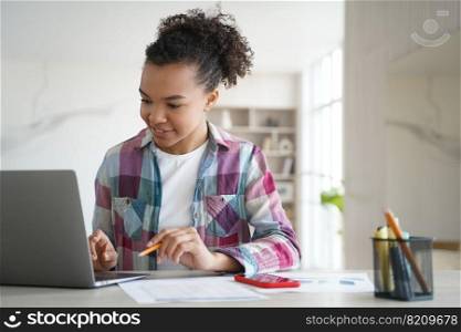 Modern mixed race teen girl student looking at laptop screen learning online at home. Smiling biracial teenager schoolgirl doing homework sitting at desk. Distance education concept.. Mixed race teen girl student looking at laptop screen learning online at home. Distance education