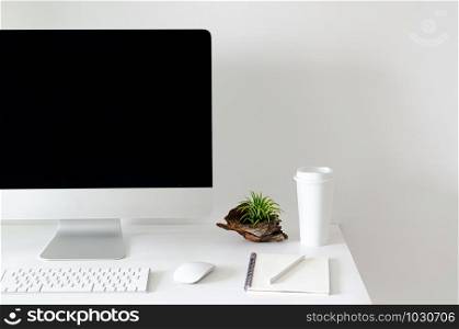 Modern personal computer screen on white table with a cup of coffee and Tillandsia air plant with space for text on white wall for working and office concept.
