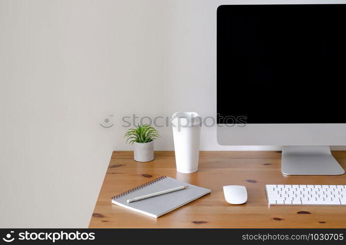 Modern personal computer screen on wooden table with a cup of coffee and Tillandsia air plant with space for text on white wall for working and office concept.