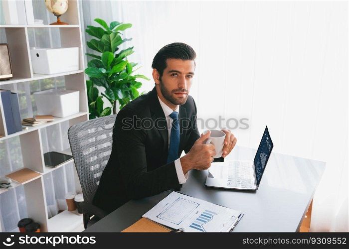 Modern professional businessman at modern office desk using laptop to work with coffee in his hand. Diligent office worker working on computer notebook in his office work space. fervent. Modern professional businessman at modern office desk with coffee. fervent