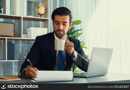 Modern professional businessman at modern office desk using laptop to work with coffee in his hand. Diligent office worker working on computer notebook in his office work space. fervent. Modern professional businessman at modern office desk with coffee. fervent