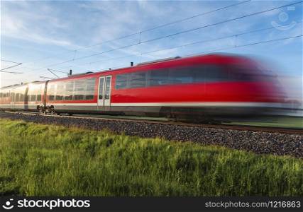 Modern red train, in motion blur, traveling through green nature, german countryside, on summer sunny day, Schwabisch Hall, Germany. Train transport.