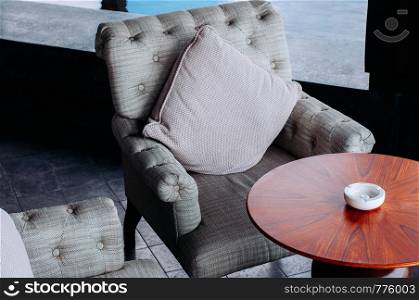 Modern retro grey fabric armchair and pillow with wooden coffee table and ash tray close up detail shot - interior decoration furniture