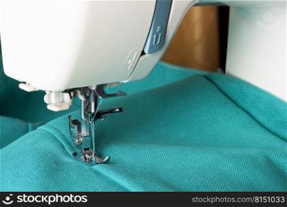 Modern sewing maχ≠working with turquoise fabric. Sewing process. Copy space.. Modern sewing maχ≠and turquoise fabric