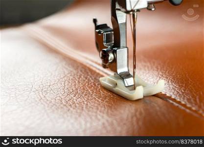Modern sewing machine presser foot with a needle sews brown leather. Sewing process of decorative seam on leatherette with special leather presser foot. Close up, copy space.. Modern sewing machine presser foot with a needle sews brown leather