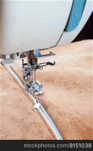 Modern sewing machine sews on the zipper on biege item of clothing. sewing process. modern sewing machine presser foot and zipper