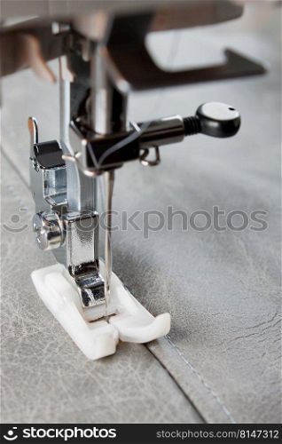 Modern sewing machine with special presser foot makes a seam on grey leather. sewing process close up. Modern sewing machine presser foot and item of clothing