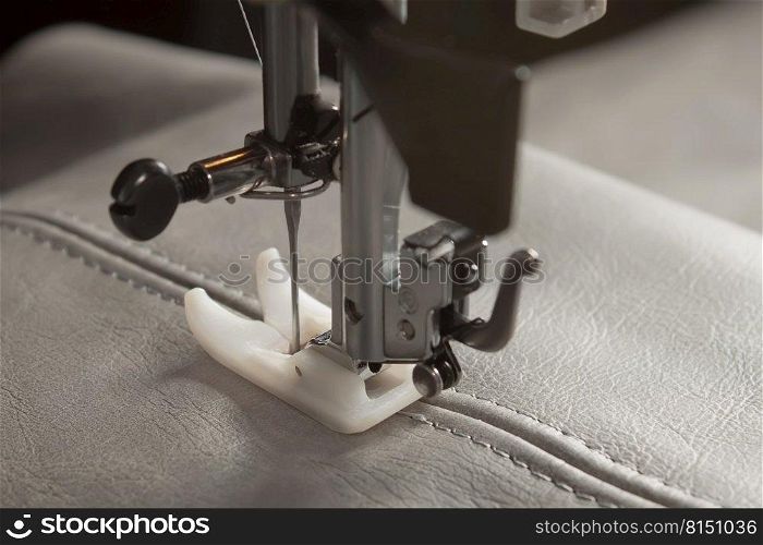 Modern sewing machine with special presser foot makes a seam on grey leather. sewing process close up. Modern sewing machine presser foot and item of clothing