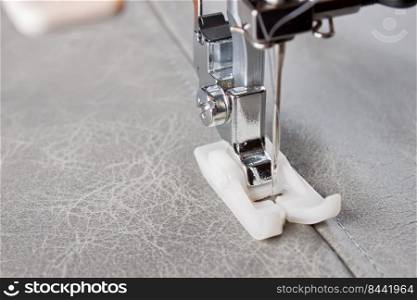 Modern sewing machine with special presser foot makes a seam on grey leather. sewing process close up, copy space. Modern sewing machine presser foot and item of clothing