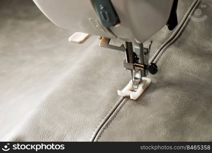 Modern sewing machine with special presser foot makes a seam on grey leather. sewing process close up, copy space. Modern sewing machine presser foot and item of clothing