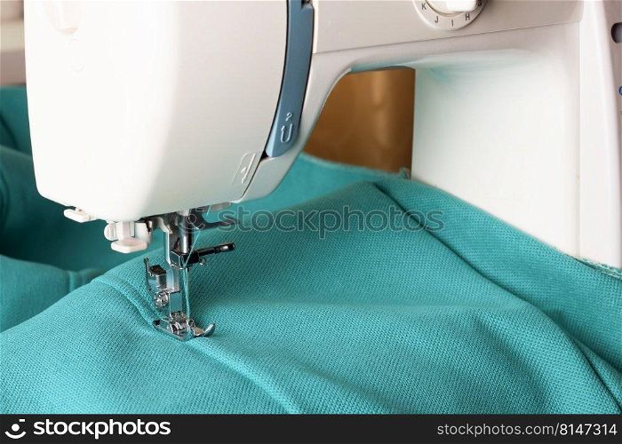 Modern sewing machine working with turquoise fabric. Sewing process. Copy space.. Modern sewing machine and turquoise fabric