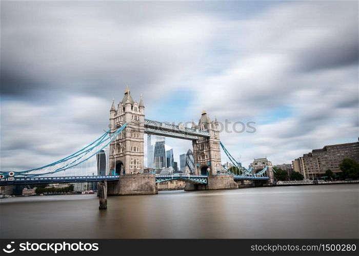Modern skyscrapers of The City of London as seen from the South shore of the river Thames through the Tower Bridge on a cloudy Summer day. Long exposure.