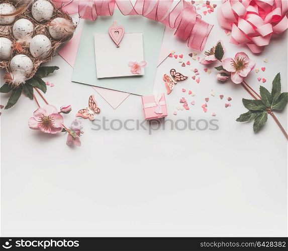 Modern styled Easter background with pastel color decoration: eggs, ribbon, flowers, bow and gift box. Mock up for Easter greeting card on white desk background, top view