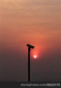 Modern surveillance camera in the foreground The orange sun shing bright before the sun was setting. The concept of surveillance evening time, copy space, Selective focus.