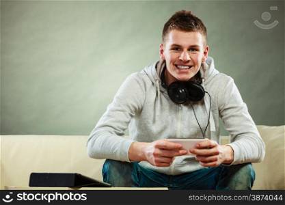 Modern technologies connection leisure concept. Young handsome man relaxing on couch with headphones smartphone and tablet at home