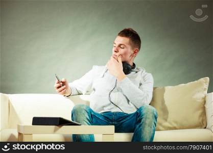 Modern technologies connection leisure concept. Young handsome man relaxing on couch with headphones smartphone and tablet at home