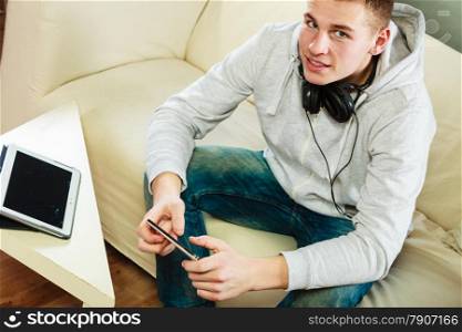 Modern technologies connection leisure concept. Young man relaxing on couch with headphones smartphone and tablet at home unusual view