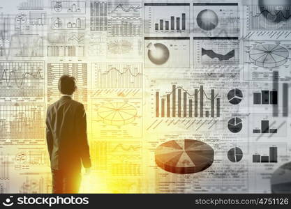 Modern technologies in business. Rear view of businessman with suitcase and diagrams on virtual panel