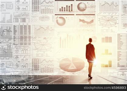 Modern technologies in business. Rear view of businesswoman with suitcase and diagrams on virtual panel
