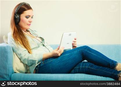 Modern technologies leisure and lifestyle concept. Young attractive woman with headphones sitting on couch using tablet