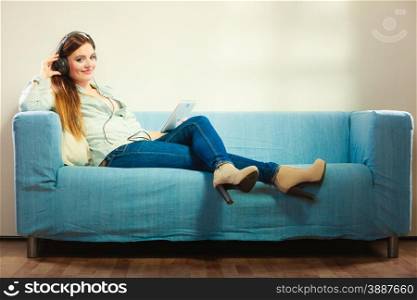 Modern technologies leisure and lifestyle concept. Young attractive woman with headphones sitting on couch using tablet