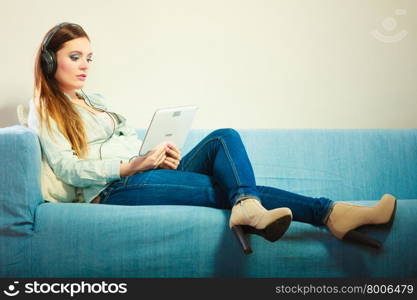 Modern technologies leisure and lifestyle concept. Young attractive woman with headphones sitting on couch using tablet