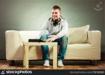 Modern technologies leisure and lifestyle concept. Young handsome man with headphones sitting on couch with tablet at home