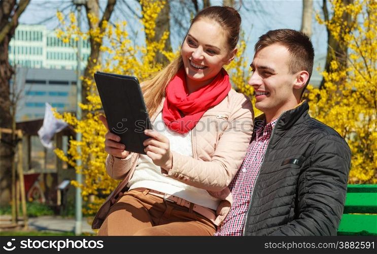Modern technologies leisure and relationships concept. Young couple with pc computer tablet sitting on bench outdoor websurfing on internet