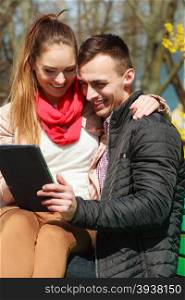 Modern technologies leisure and relationships concept. Young couple with pc computer tablet sitting on bench outdoor websurfing on internet