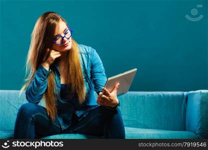 Modern technologies leisure and young people concept. fashionable woman wearing jeans with tablet sitting on couch blue color